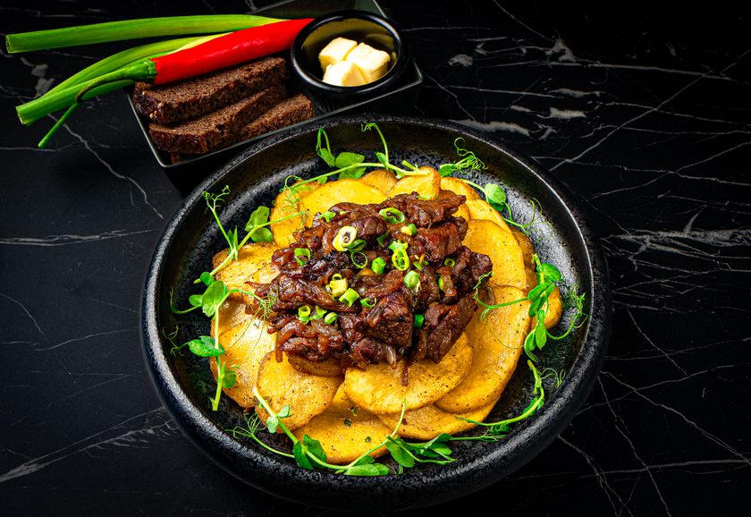 Braised beef over sliced sauteed potatoes with spring onion, rye bread and butter alongside