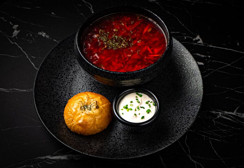 Borscht in a dark bowl with sour cream and a bread roll