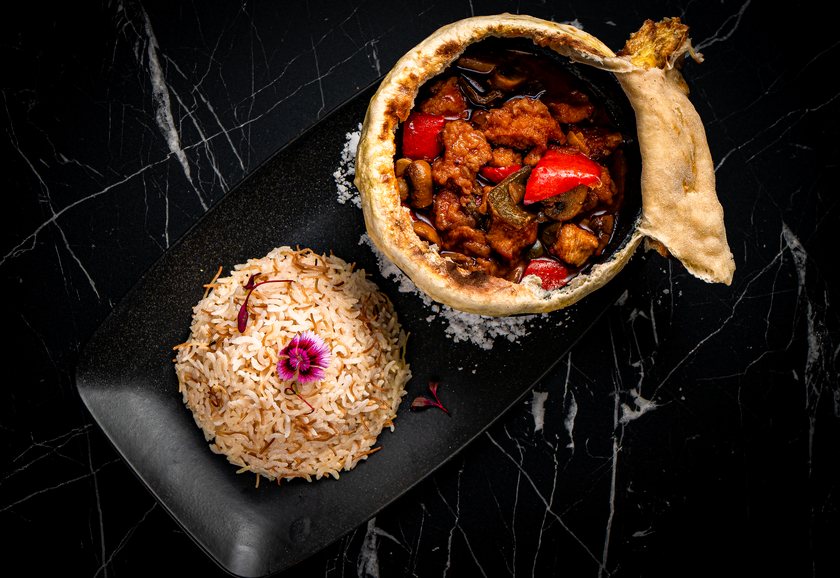 Testi kebab in a clay pot sealed with bread, opened to show meat with peppers and mushrooms, served with rice