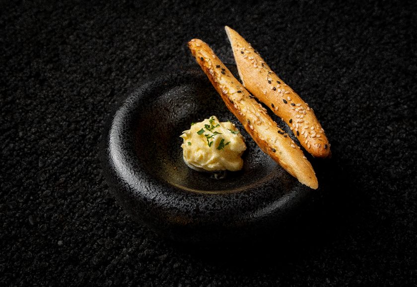 Two seeded bread sticks with a quenelle of whipped butter in a stone bowl