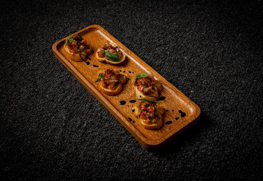 Five bruschetta topped with chopped tomato and basil on a wooden board