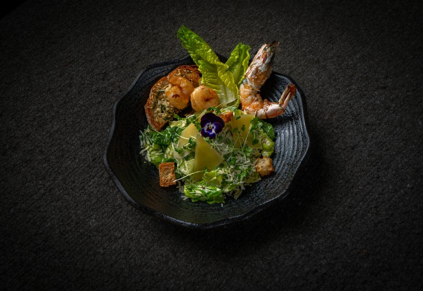 Caesar salad with grilled prawns, parmesan and croutons in a dark bowl