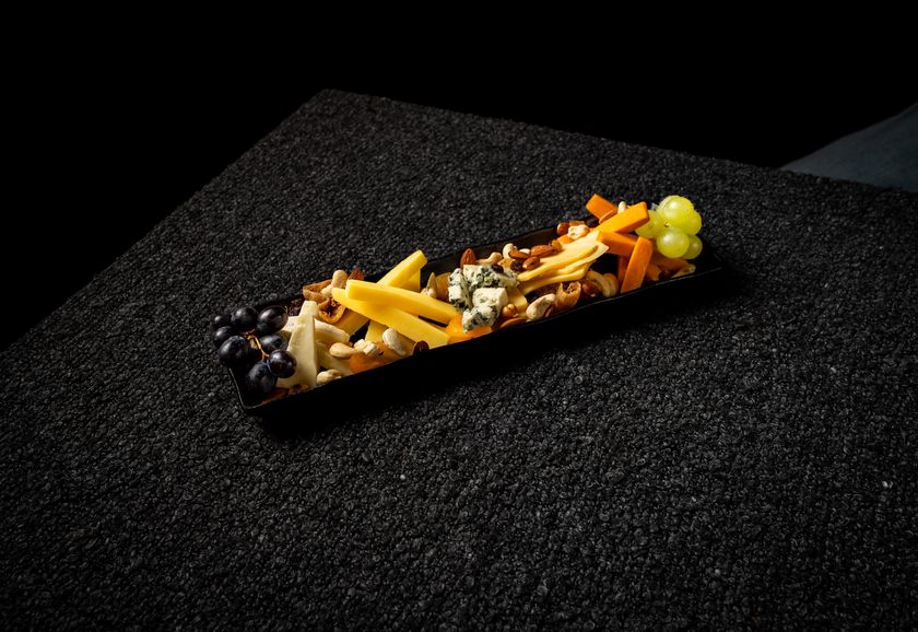A long slate board of assorted cheeses with nuts, dried fruit and grapes