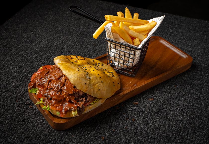 A beef doner sandwich in flatbread with a basket of fries