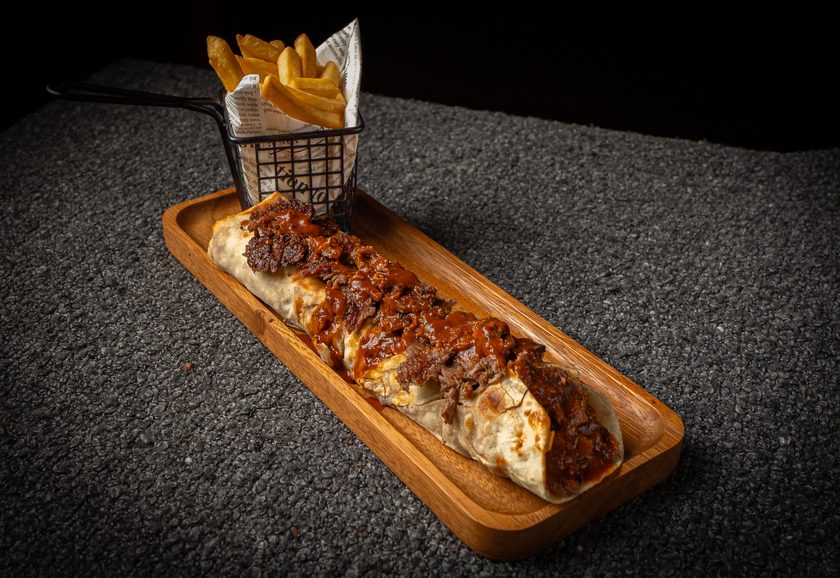 A beef durum wrap on a wooden board with a basket of fries