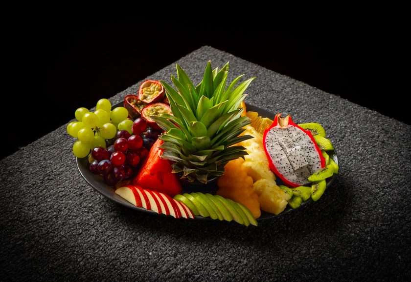 A platter of sliced seasonal fruit around a whole pineapple crown