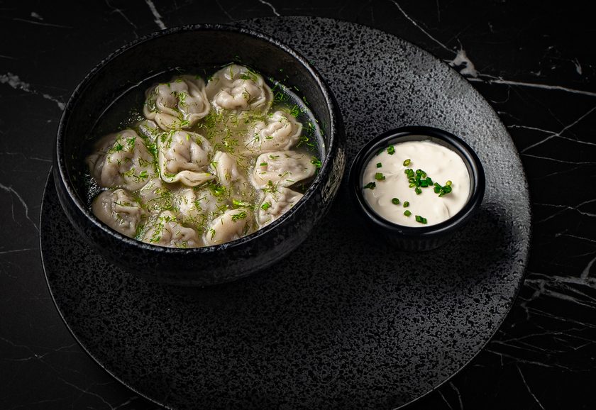 Pelmeni dumplings in a dark bowl with sour cream