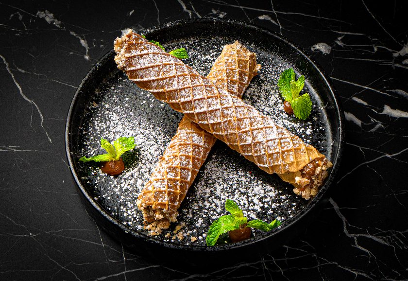 Two crisp waffle tubes filled with cream, dusted with icing sugar